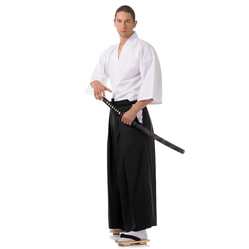 Puede incluir: Una persona que lleva un uniforme blanco de artes marciales con un cintur&oacute;n negro y sostiene una katana.
