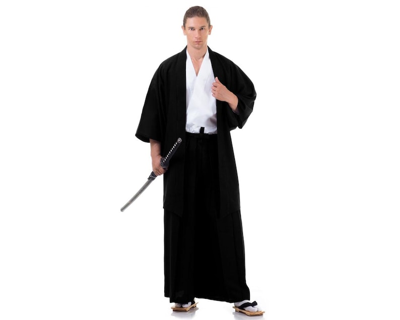 Puede incluir: Una persona vestida con un kimono negro y sosteniendo una katana. El kimono tiene una prenda interior blanca y una faja negra.