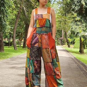 May include: A colorful patchwork jumpsuit with a wide leg silhouette. The jumpsuit is made of various fabrics in shades of orange, green, blue, and brown. The straps are thin and have a ruffled detail.