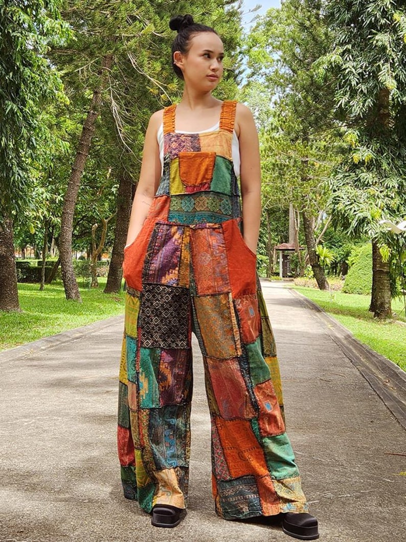 May include: A colorful patchwork jumpsuit with a wide leg silhouette. The jumpsuit is made of various fabrics in shades of orange, green, blue, and brown. The straps are thin and have a ruffled detail.