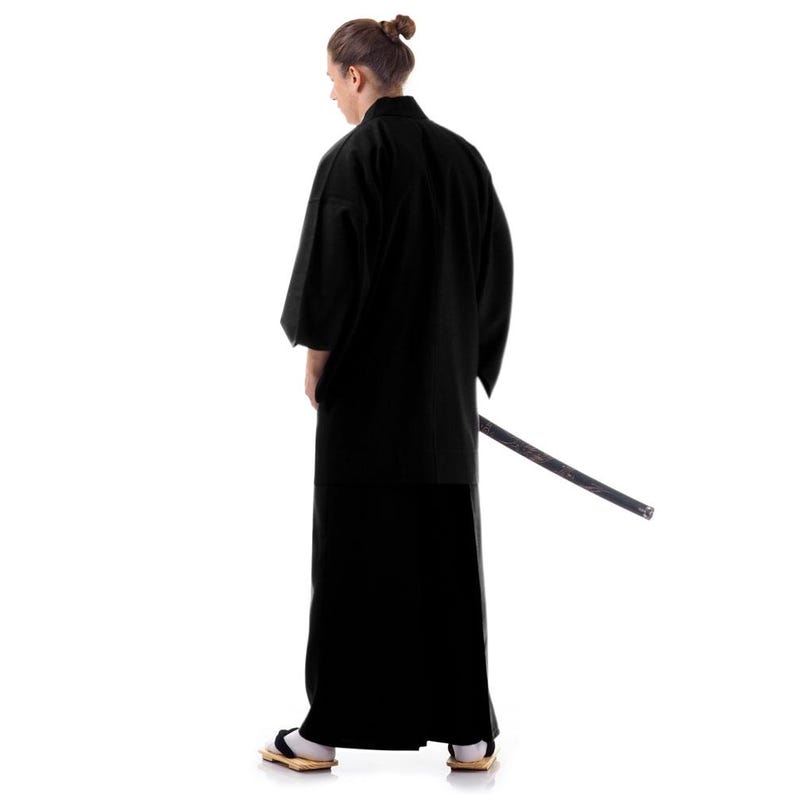 Puede incluir: Una persona vestida con un kimono negro y pantalones negros, de pie de espaldas a la c&aacute;mara. Sostiene una espada negra en su mano derecha.