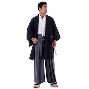 Op de afbeelding: Een man draagt een zwarte kimono met een wit onderhemd en een grijze broek. Hij houdt een zwaard in zijn rechterhand.