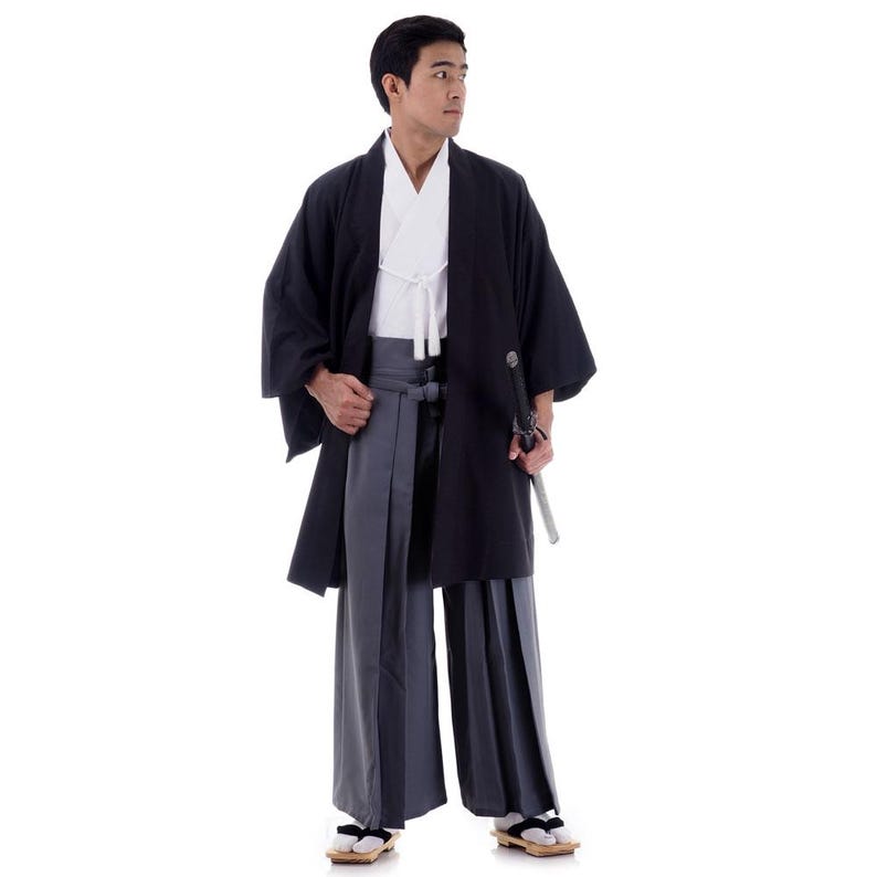 Op de afbeelding: Een man draagt een zwarte kimono met een wit onderhemd en een grijze broek. Hij houdt een zwaard in zijn rechterhand.