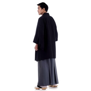 May include: A person wearing a black kimono with a grey hakama, a traditional Japanese outfit.