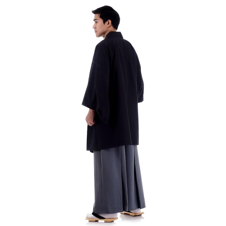 May include: A person wearing a black kimono with a grey hakama, a traditional Japanese outfit.