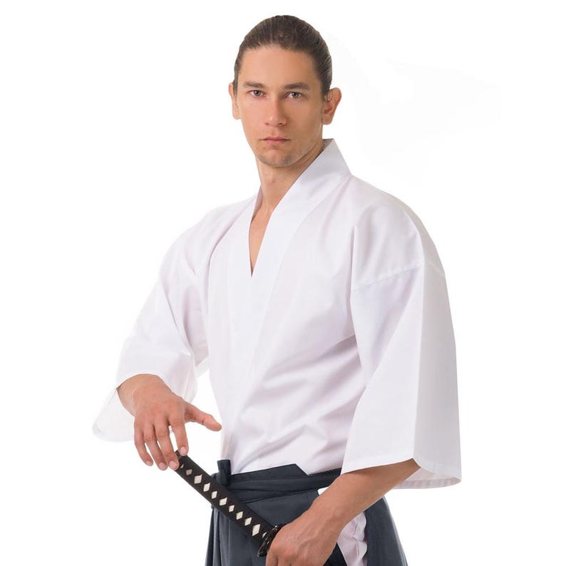 Op de afbeelding: Een persoon die een wit martial arts uniform draagt met een zwarte band en een zwaard vasthoudt.