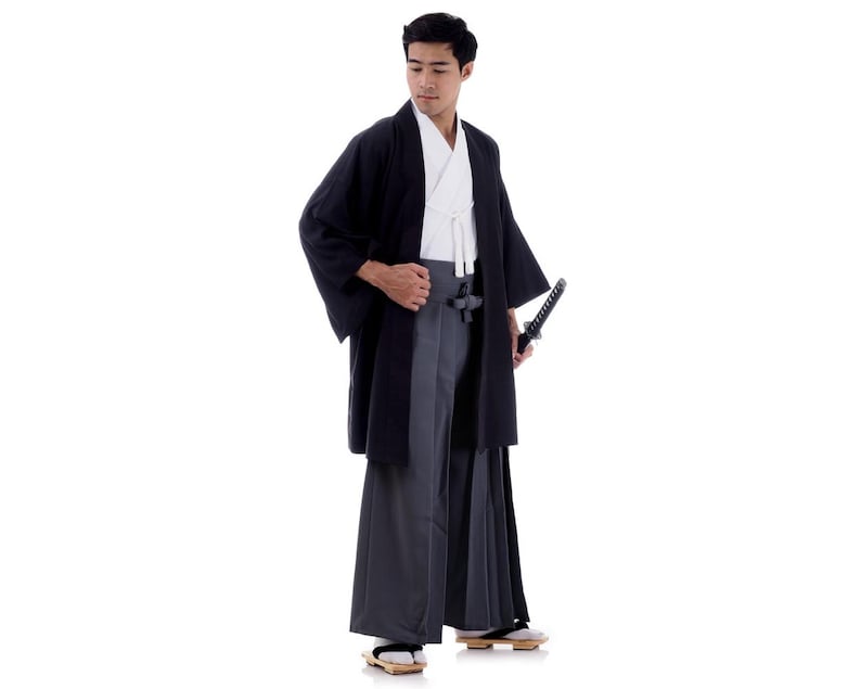 Op de afbeelding: Een man die een zwarte kimono draagt met een wit onderkleed en een zwaard. Hij staat met zijn hoofd gebogen en houdt het zwaard in zijn rechterhand.