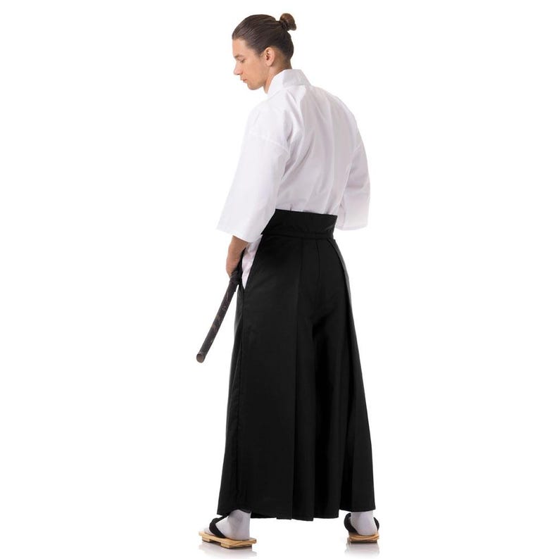 Puede incluir: Una persona que lleva un uniforme blanco de artes marciales con un cintur&oacute;n negro y pantalones negros. Est&aacute; sosteniendo una espada de madera en su mano derecha.