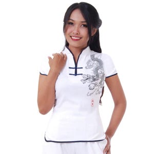 May include: White short-sleeved shirt with a mandarin collar and a black dragon design. The shirt has a navy blue trim and two buttons on the collar.