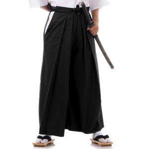 Puede incluir: Pantal&oacute;n negro de piernas anchas con una cintura blanca y una raya blanca a los lados. El pantal&oacute;n se lleva con una camiseta blanca y una espada negra.
