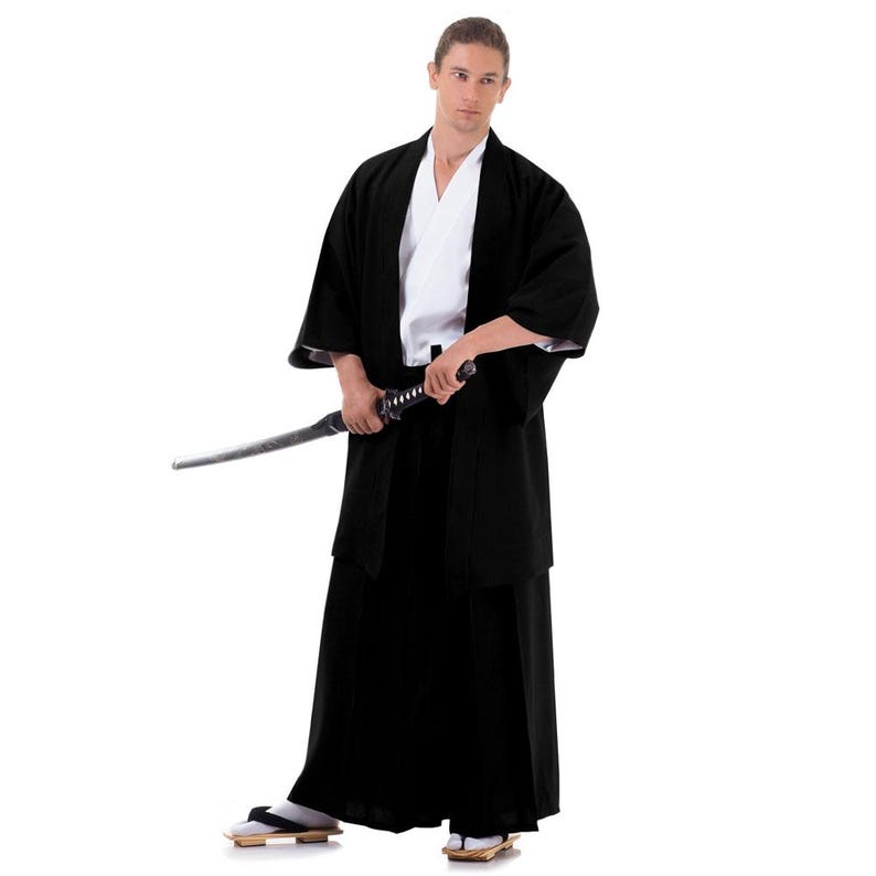Puede incluir: Una persona vestida con un kimono negro y hakama, sosteniendo una katana. El kimono tiene un cuello blanco y est&aacute; atado con una faja negra. La persona est&aacute; de pie sobre un fondo blanco.