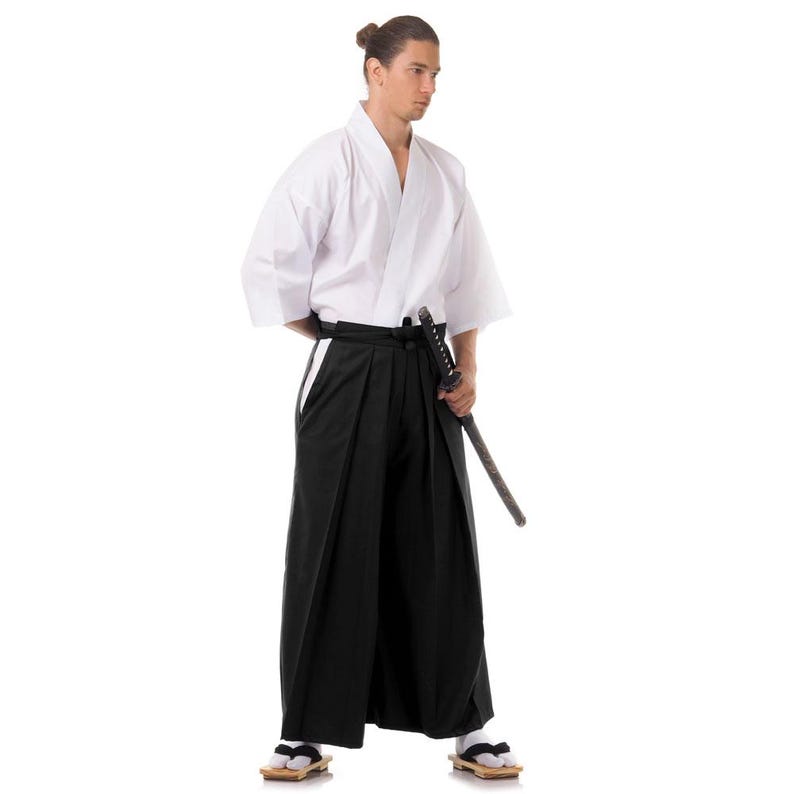 Puede incluir: Una persona vestida con un uniforme blanco de artes marciales con un cintur&oacute;n negro y una espada. La persona est&aacute; de pie con los pies separados y las manos en la espada.