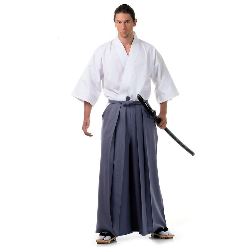 Op de afbeelding: Een persoon draagt een witte kimono met een grijze hakama en een zwart zwaard.