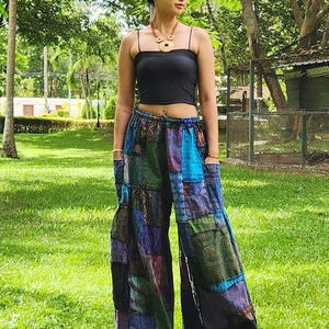 May include: A woman wearing a black tank top and patchwork pants with a variety of colors and patterns. The pants have a wide leg and are made of a soft, flowing fabric.