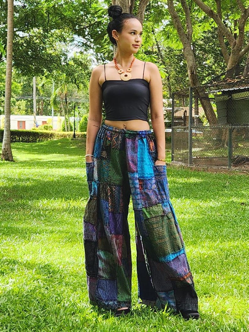 May include: A woman wearing a black tank top and patchwork pants with a variety of colors and patterns. The pants have a wide leg and are made of a soft, flowing fabric.