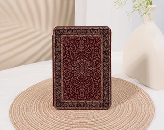 May include: A rectangular, burgundy-colored decorative item with an intricate floral pattern, resembling a miniature rug. The item is placed on a round, woven placemat. The background includes a white vase with flowers.