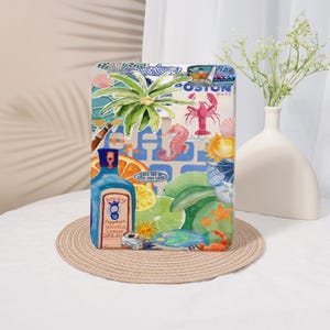 May include: A rectangular decorative sign featuring a vibrant collage of coastal and summer-themed illustrations, including a blue gin bottle, a lobster, a seahorse, citrus slices, a palm leaf, and various seashells against a light background.