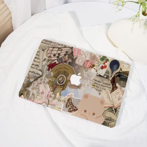May include: A decorative laptop skin featuring a collage of vintage elements. The design includes sheet music, floral accents, a teddy bear illustration, and the text "LOVE". The Apple logo is visible in the center.