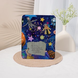 May include: A colorful tablet case featuring a whimsical design with stars, buttons, and cartoon characters. The case has a dark blue background with the text "hey Jonesy, Look what I found in Gramma's trunk, Look familiar? Wybie."