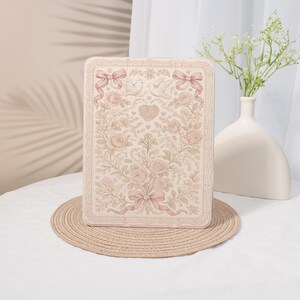 May include: A rectangular tablet case featuring a soft pink and cream colour palette with a detailed illustration of two doves, a central heart, blooming roses, and decorative bows, all framed by a delicate lace-like border pattern.