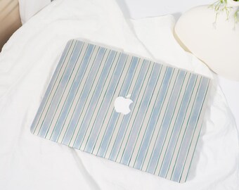 Może przedstawiać: Etui na laptopa z niebiesko-białym wzorem w paski. Etui ma białe logo Apple pośrodku. Prostokątne etui wydaje się być wykonane z twardego materiału.