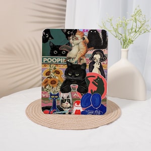 May include: A rectangular art print with a collage of cat illustrations. The artwork includes various cat depictions, such as black cats, ginger cats, and cats with human-like features. The word "POOPING" is visible in the upper left corner. The print is displayed on a beige woven mat.