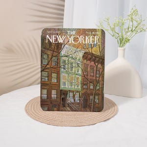 May include: A decorative tablet featuring a vintage cover of The New Yorker magazine. The cover art depicts a colourful illustration of brownstone buildings with bare trees. The tablet is resting on a round, woven placemat.