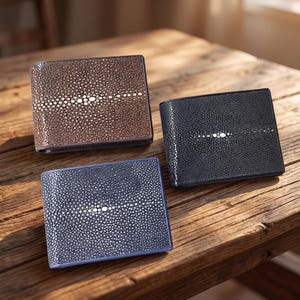 May include: Three bifold wallets featuring a textured stingray leather surface. Each wallet displays a distinct central horizontal band of larger, lighter-coloured, rounded nodes. The set includes one brown, one black, and one blue wallet.