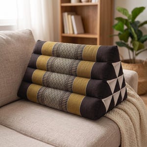 May include: A triangular-shaped floor cushion featuring a repeating pattern of dark brown, olive green, and cream-colored fabric panels. The cushion has a structured, multi-sectioned design with intricate geometric embroidery on the central bands.