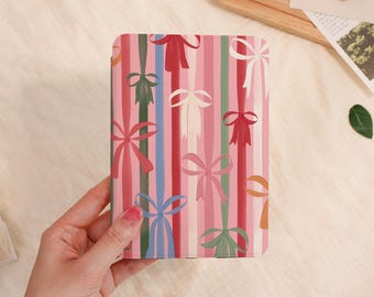 May include: A pink tablet case with a colorful bow and stripe pattern. The design features vertical stripes in shades of pink, red, blue, and green, with bows of various colors. The case is held by a person.