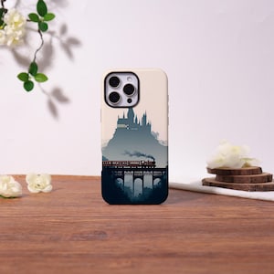 May include: A cream-colored smartphone case featuring a graphic illustration of a dark silhouette of a castle perched on a mountain above a steam train crossing a stone viaduct, with a dark blue gradient fading into the base of the phone case.