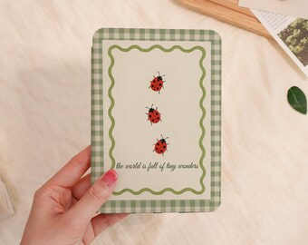 May include: A rectangular case with a green and white gingham border and a scalloped green inner frame. The centre features three red ladybirds and the text "the world is full of tiny wonders."