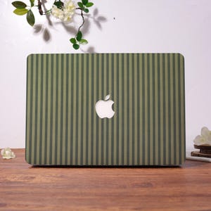 Könnte beinhalten: Eine Laptop-Hülle mit einem vertikalen Streifenmuster in abwechselnden Farbtönen von Olivgrün und dunklem Waldgrün. Das Design enthält einen mittigen Ausschnitt, der das weiße Apple-Logo auf dem Laptop-Deckel freilässt und ein einheitliches Bild ergibt.