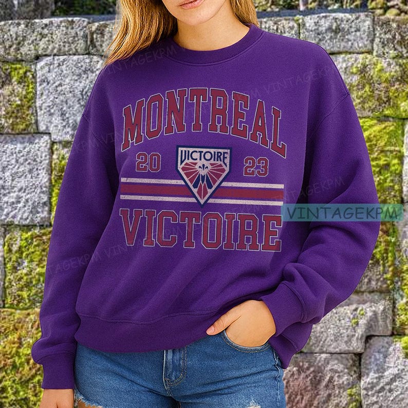 May include: A purple sweatshirt with the word "MONTREAL" arched across the top in white and red lettering. Below, the text "20 VICTOIRE 23" is displayed above a crest. The word "VICTOIRE" is repeated at the bottom in red.