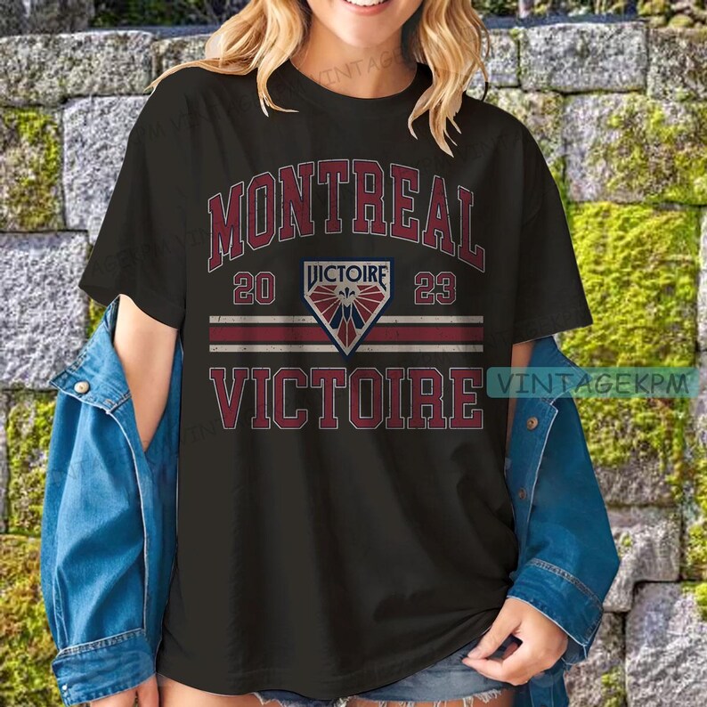 May include: Black t-shirt with the word "MONTREAL" in maroon, above "20 VICTOIRE 23" and "VICTOIRE" in maroon. The shirt has a diamond-shaped emblem with a fleur-de-lis design. The shirt is worn with a denim jacket.