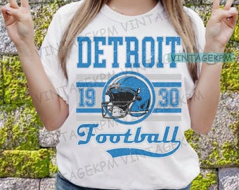 Könnte beinhalten: Weißes T-Shirt mit einem blauen und grauen Grafikdesign. Die Grafik zeigt einen Footballhelm, den Text "DETROIT" und die Zahlen "19" und "30". Der Text "Football" ist in einer blauen, geschwungenen Schrift geschrieben.