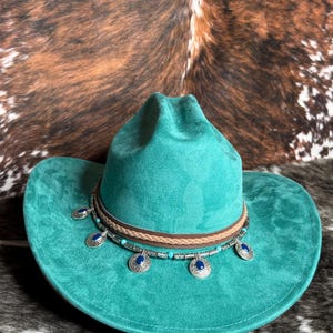 May include: A turquoise cowboy hat with a brown leather band and decorative silver and blue embellishments. The hat has a wide brim and a classic western design, perfect for adding a touch of country style.
