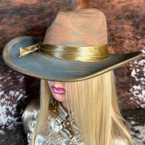 May include: A wide-brimmed hat with a blue and brown crown and a gold band. The hat is made of felt and has a slightly distressed look.