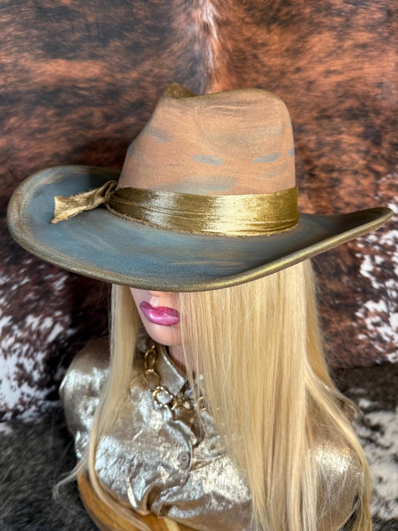 May include: A wide-brimmed hat with a blue and brown crown and a gold band. The hat is made of felt and has a slightly distressed look.