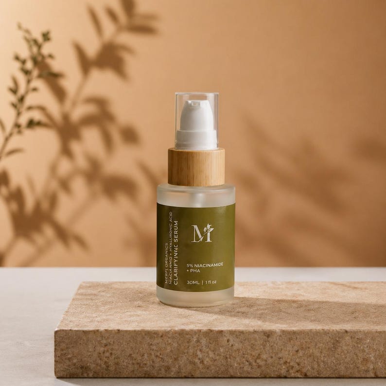 May include: A clear glass serum bottle with a white pump and wooden collar. The label reads "MIFU ORGANICS CLARIFYING SERUM" and includes the text "5% NIACINAMIDE + PHA". The bottle is on a stone surface with a neutral background.
