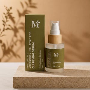 May include: A skincare product set with a green box and a clear glass bottle. The box and bottle display the text "MERFU ORGANICS CLARIFYING SERUM" with the ingredients listed. The bottle has a wooden cap and a white pump.