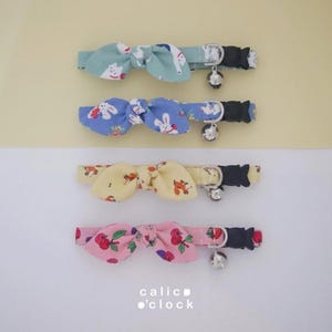 Peut inclure: Quatre colliers pour chats avec des nœuds papillon à motifs dans des tons pastel : vert menthe, bleu, jaune et rose. Chaque collier est orné d'une clochette argentée et d'une boucle noire. Les nœuds présentent des motifs de lapin, de renard et de cerise.
