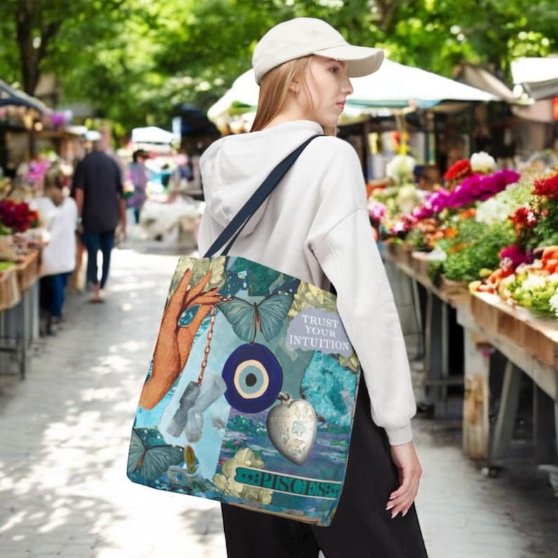 May include: A teal tote bag with a collage design featuring butterflies, a hand, an evil eye, and a heart-shaped pendant. The text "TRUST YOUR INTUITION" and "PISCES" are also visible. The bag has a navy blue strap.