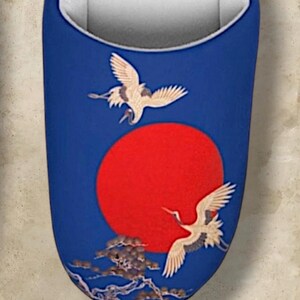 May include: Blue slipper with a red sun and two cranes in flight. The design includes a detailed illustration of the birds and a stylized landscape. The interior is white.