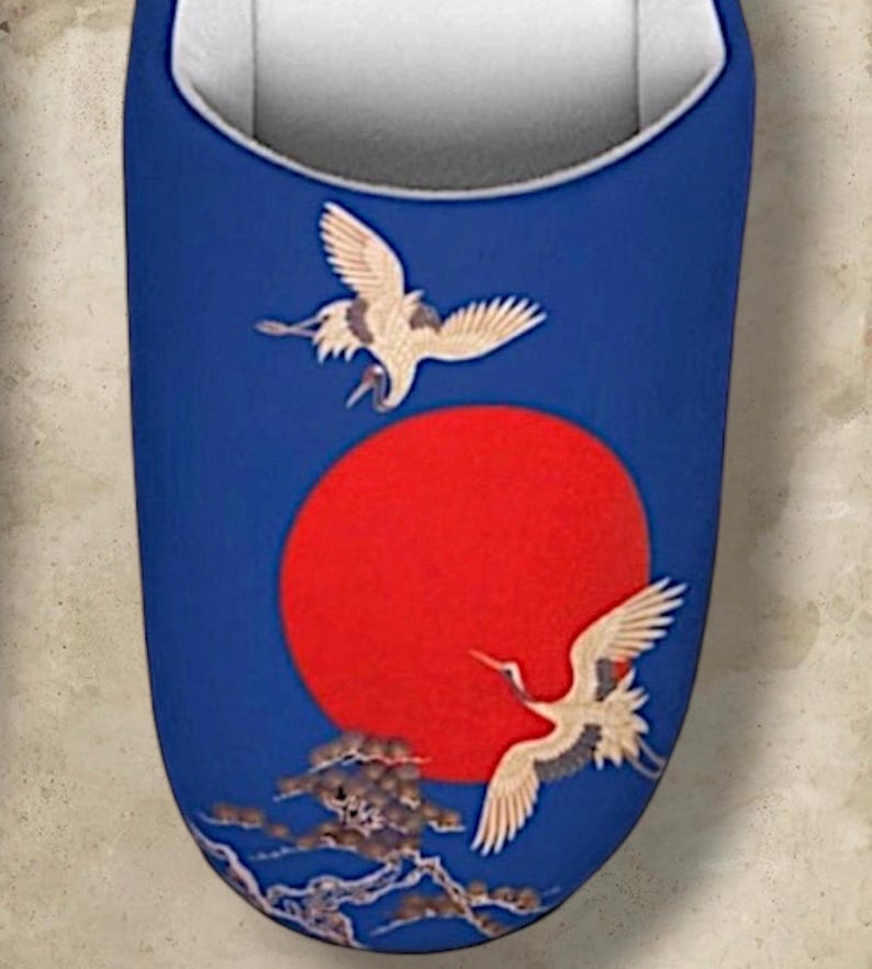 May include: Blue slipper with a red sun and two cranes in flight. The design includes a detailed illustration of the birds and a stylized landscape. The interior is white.
