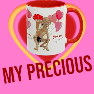 May include: A white ceramic mug with a red rim and handle. The mug features a cartoon illustration of Gollum from the Lord of the Rings holding a bouquet of red flowers and surrounded by pink heart-shaped balloons. The text "You are my precious" is written on the mug.