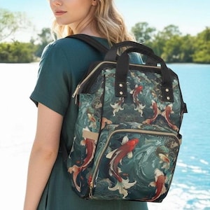 Könnte beinhalten: Ein tealfarbener Rucksack mit einem Koi-Fisch-Design. Der Rucksack hat einen schwarzen oberen Griff und Träger, mit einer Vordertasche und Seitentaschen. Die Koi-Fische sind rot, weiß und goldfarben auf tealfarbenem Hintergrund.
