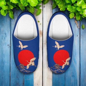 May include: A pair of blue slippers with a Japanese-inspired design. Each slipper features a red sun, flying cranes, and a landscape scene. The interior is white.