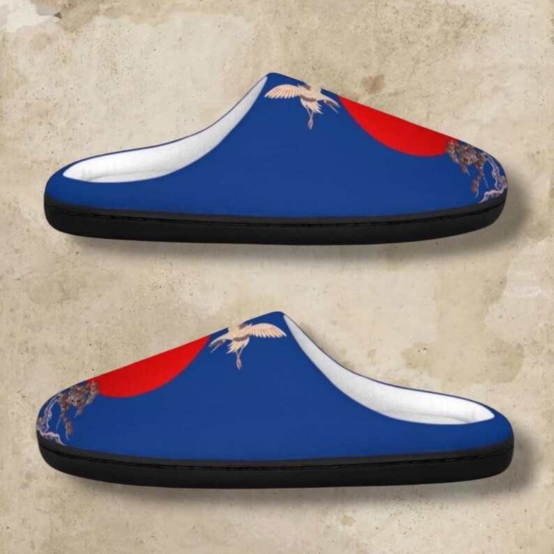 May include: A pair of blue slippers with a white interior and black soles. Each slipper features a red circle and a crane design. The slippers are designed for indoor use.