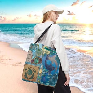 May include: A tote bag with a blue and teal design featuring a Pisces theme. The bag has a black shoulder strap and a variety of images, including a ring, a butterfly, and two fish. The bag is being carried on a beach.